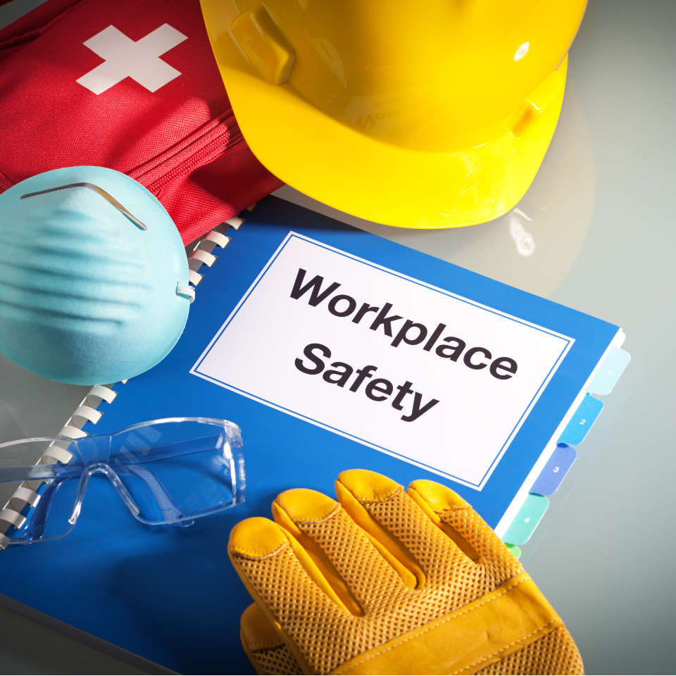 Workplace safety handbook with occupational safety equipment still life, a work training class and instruction manual for using safety equipment and administering first aid. Employment education document with protective eyewear, hard hat, first aid kit, work glove, and pollution mask. Guidance and planning tools in horizontal format with copy space.